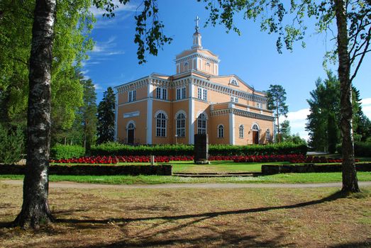 Rautala Church of Rautalampi city in the main plane,  the military cemetery of 1913 decorated with red flowers is foreground, the complx is surrounded by the park, it is the province of Eastern Finland, part of the Northern Savonia region