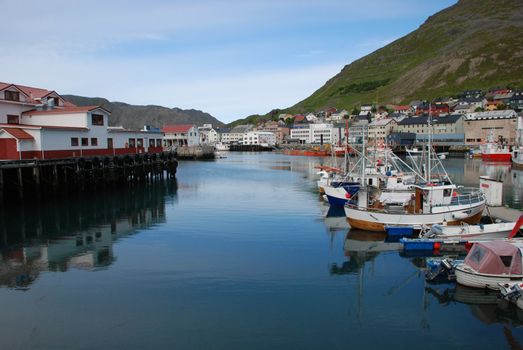 Its a port and cityscape of Honningsvag, one of the northernmost city in Norway and  in the world,  fishers and indusctrial vessels are at biggest port of Mageroya Island, with the buildings, houses and desert hill at background