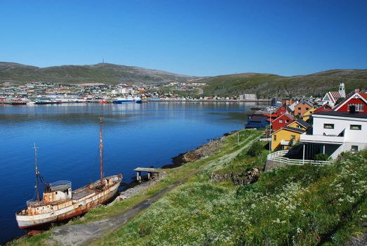 Its a cityscape of Hammerfest, claimed as a northernmost city in the world, the top of city church is behind of houses colored with different colours of Finnmark country and old vessel in the border of see