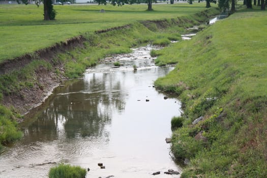 a small creek next to a grassy hill.