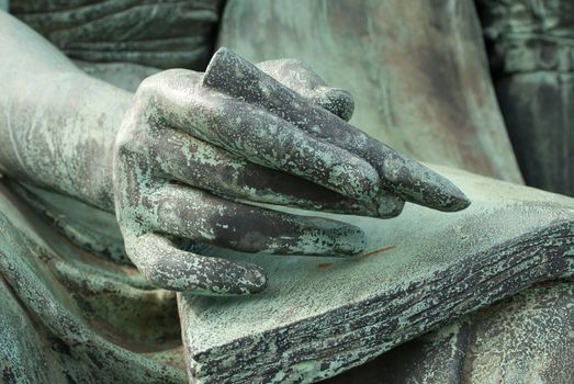 a detail of a sculpted hand writing with a pencil on a paper