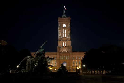 The Berlin Town Hall (Rotes Rathaus) in Germany with the silhouette of the Neptune fountain in the foreground.