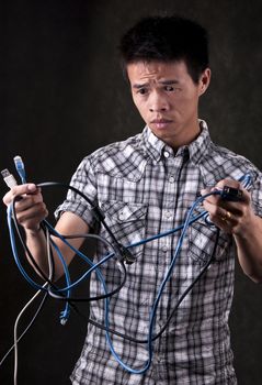 Asian Man holding computer cables looking very confused and frustrated
