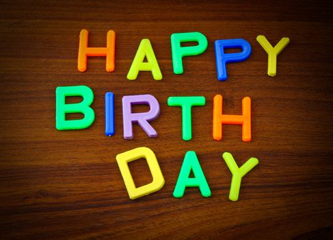 Happy Birthday in colorful toy letters on wood background