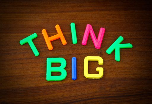 Think big in colorful toy letters on wood background