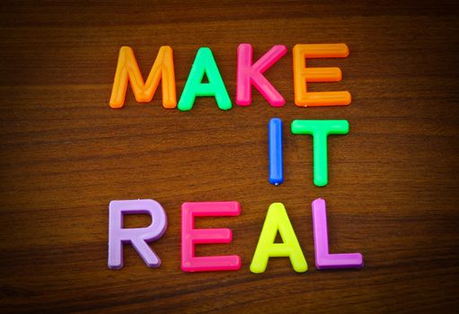 Make it real in colorful toy letters on wood background
