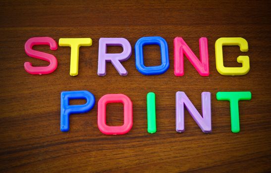 Strong point in colorful toy letters on wood background