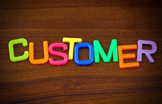 Customer in colorful toy letters on wood background