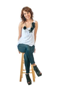 Pretty young brunette smiles as she rests on a stool. Isolated on white background. Plenty of copy space