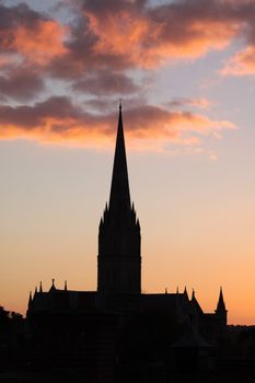 A winter sunset over Salisbury Cathedral in the city of Salisbury, Wiltshire. The cathedral silhouetted against low winter clouds. Set on a portrait format.