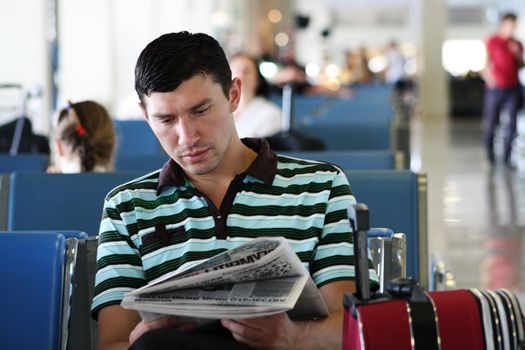 Man reading newspaper at the airport in the sitting