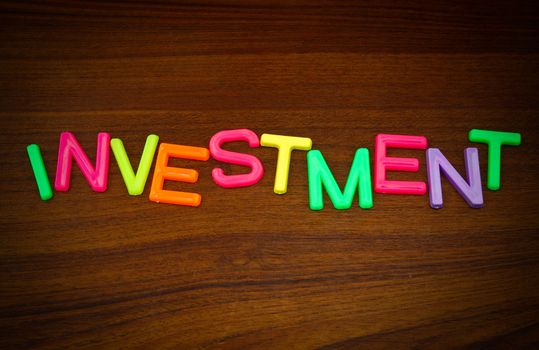 Investment in colorful toy letters on wood background