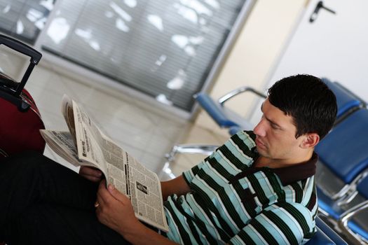 Man reading newspaper at the airport in the sitting