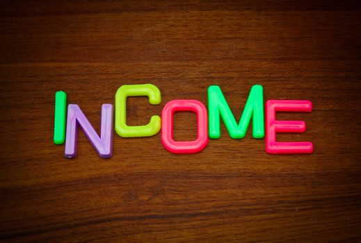 Income in colorful toy letters on wood background