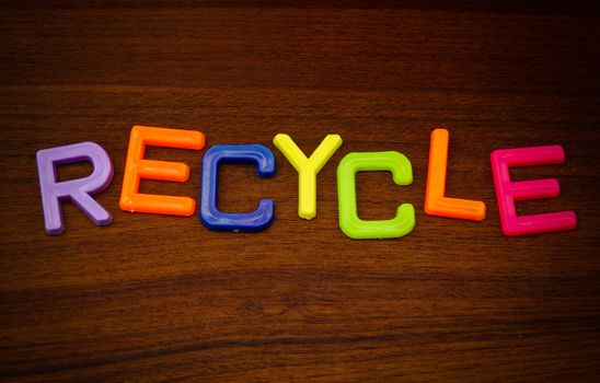 Recycle in colorful toy letters on wood background