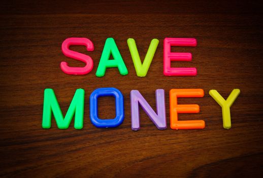 Save money in colorful toy letters on wood background