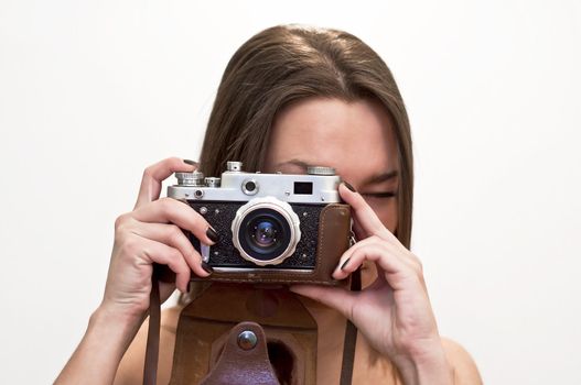 Young woman looks at an old film camera. Studio shot on white background.
