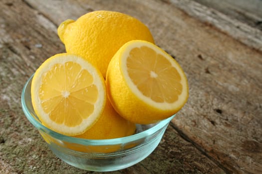 A bowl of fresh lemons with one cut in half.