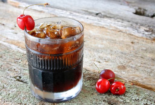 A glass of cherry soda and ice cubes with fresh ripe cherries as a garnish.