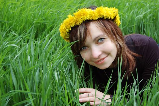 Girl with dandelion diadem over green grass