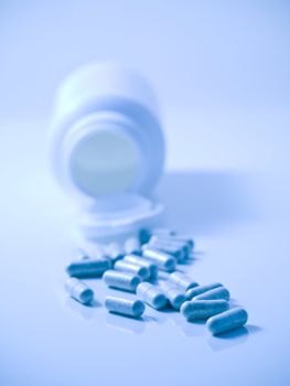 Blue tinted picture of  pills with bottle on reflective surface and with selective focus