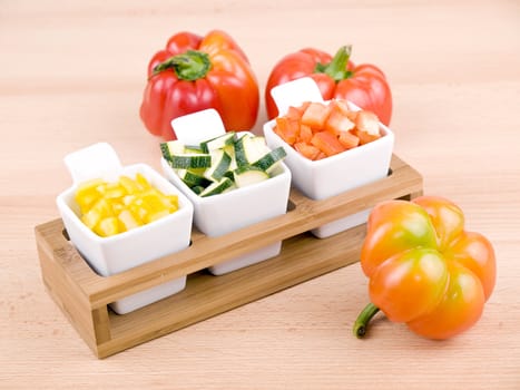 Fresh choped paprika and zucchini in small porcelain bowls on wooden table