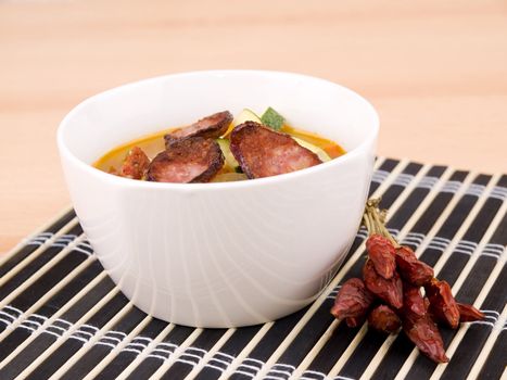 Tasty red paprika soup in white porcelain bowl on black bamboo mat.