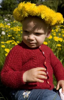 Toddler sitting in a flower field, with a yellow dandelion wreath.