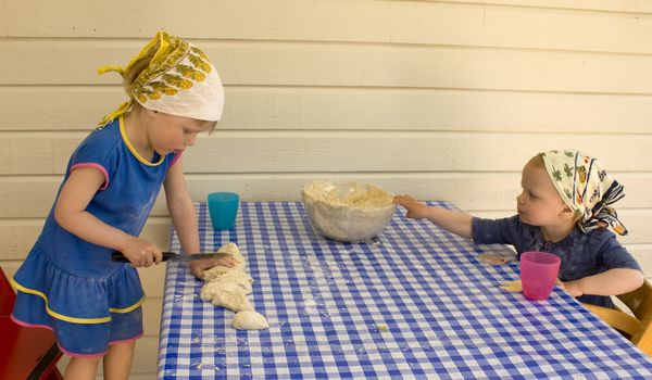 Small child (3 years old) cutting dough with a sharp knife,  toddler grabbing a heavy glass bowl. 