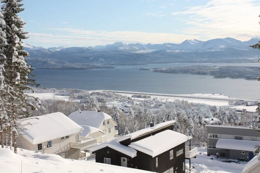 Neighbourhood of modern houses with fantastic view over fjord, islands, and mountains, in a snow clad winter landscape