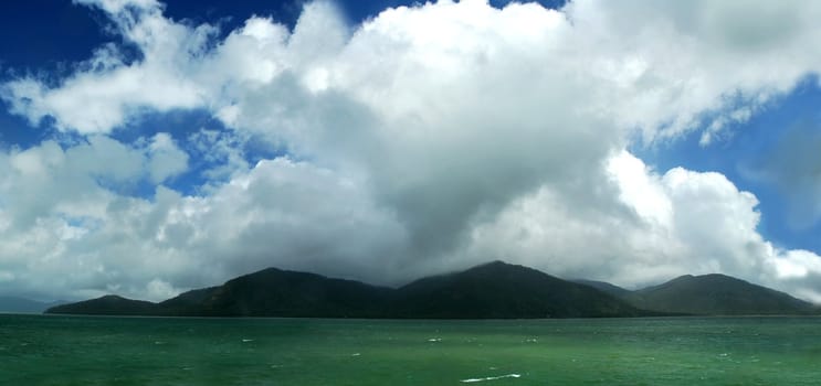 green ocean, green forest mountains, dark blue sky, clouds, ocean view