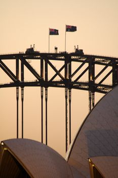 detail photo of opera house and harbour brige in sydney, two australian flags, mostly pink colour - sunset