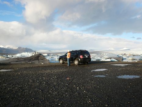 Girl next to SUV in front of Jokulsarlon, a lake in Iceland, where icebergs are floating around.