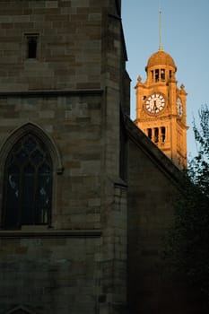 church in shadow, behind it is sun lighted clock tower - belongs to railway station in Sydney