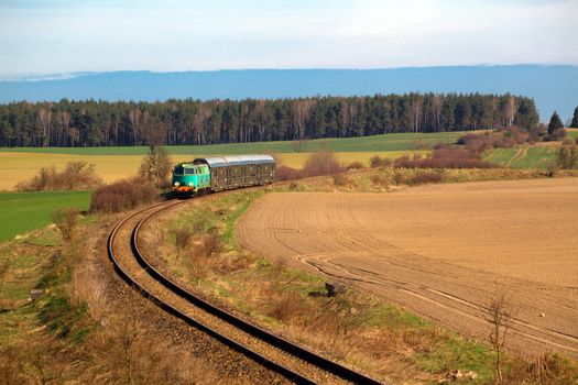 Passenger train hauled by the diesel locomotive passing the sunny landscape
