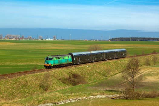 Passenger train hauled by the diesel locomotive passing the sunny landscape
