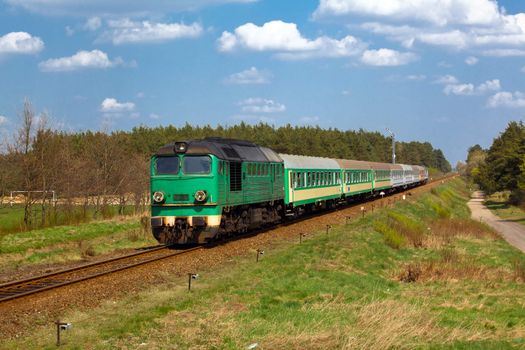 Passenger train hauled by the diesel locomotive passing the sunny landscape
