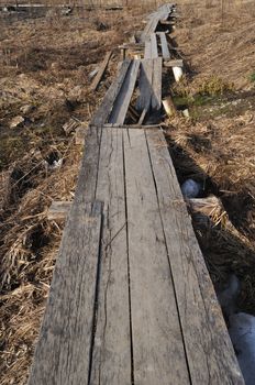 Broken wooden foot way in ravine on dry grass background