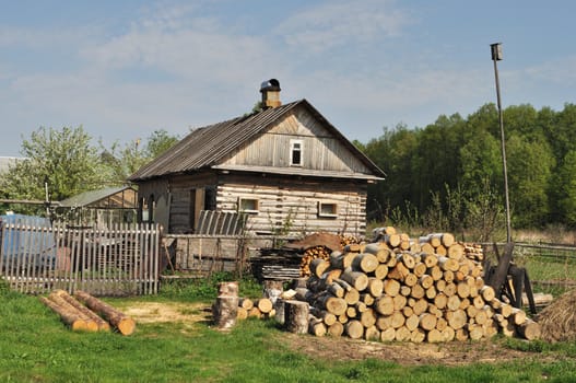Country wooden house and pile of birch chocks on foreground