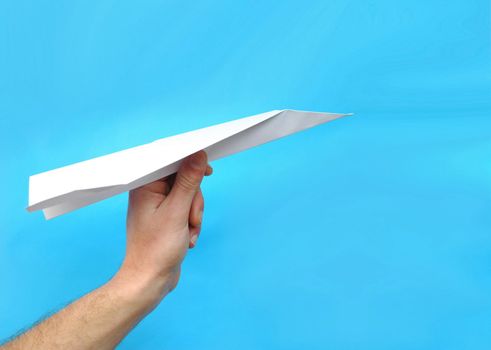 A hand holding a paper airplane on blue sky background.