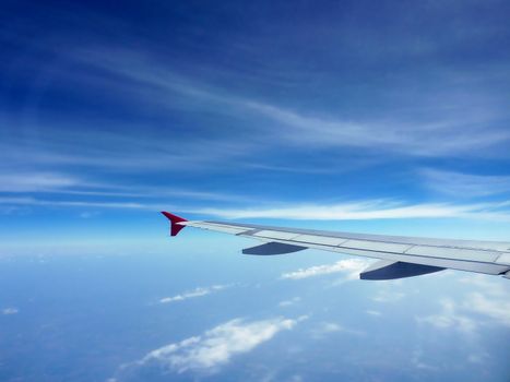 Red and grey wing of a plane flying in a beautiful cloudy blue sky