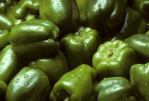 Pile of green Bell peppers with water droplets, filling frame