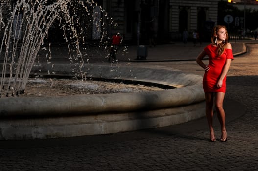 Portrait of a young attractive woman in a red dress in the city at dusk