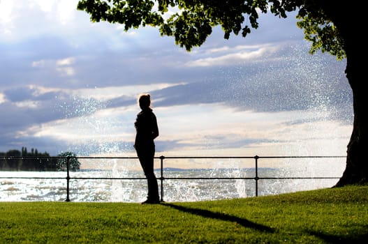 Silhouette of a young woman at the seaside standing on grass with water splashes behind