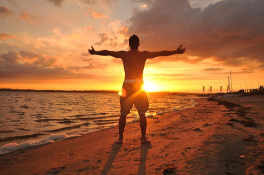 Young man with spread arms celebrating and enjoying the moment at the seaside at sunset