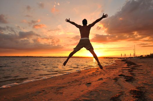 Young man with spread arms celebrating and enjoying the moment at the seaside at sunset