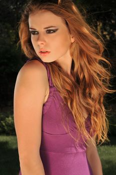 Portrait of a young attractive woman in a violet dress posing in the wind outdoors