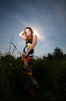 Portrait of a young attractive woman in a colorful dress posing in the sun outdoors