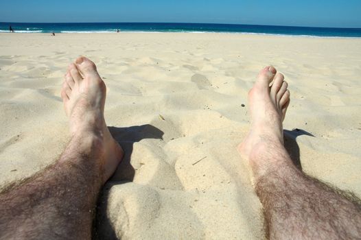 man hairy legs on beach, water and people in background