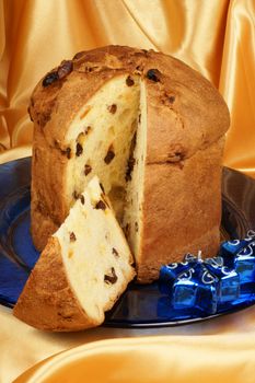 Panettone the italian Christmas fruit cake served on a blue glass plate over a yellow background and two candles. Selective focus.